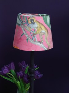 Bright pink textured lampshade depicting a rich tropical scene and monkey that looks cheeky and playful.