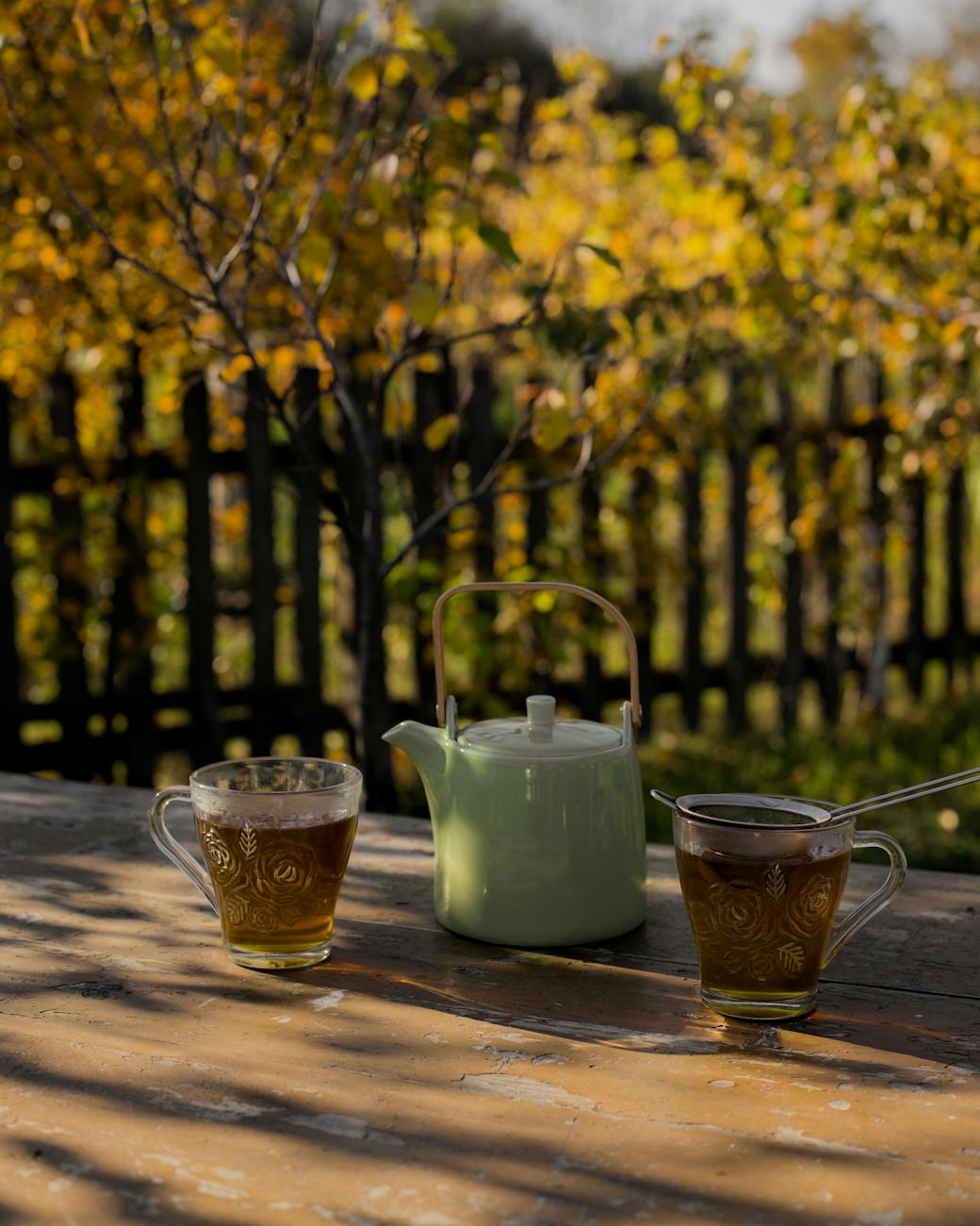 English country garden with green teapot and two cups of green brown looking tea in glass cups