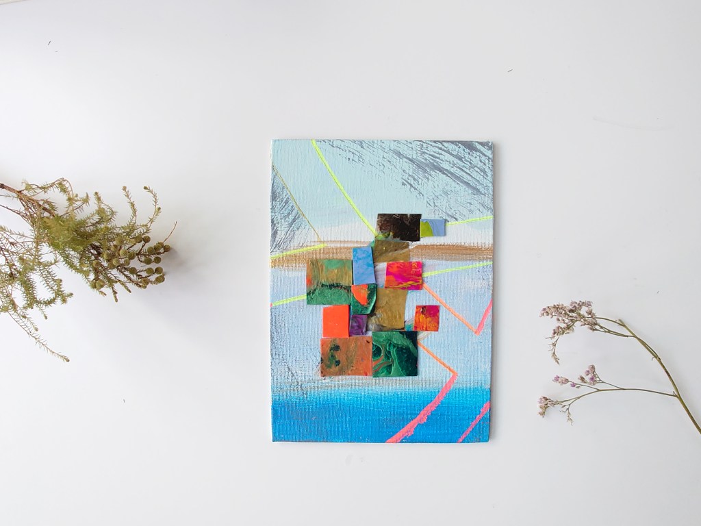 A turquoise blue, orange and gold one of a gallery of small hand painted and crafted artwork arranged with sea lavender and other flowers for a whimsical scene. Styled to show the artwork. 